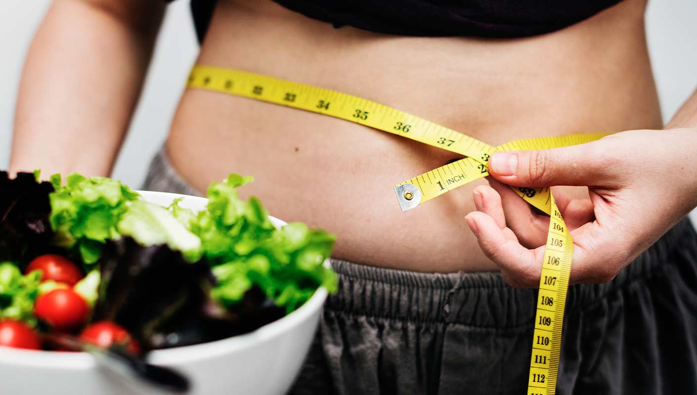 femme qui mesure son tour de taille avec une salade dans la main en premier plan