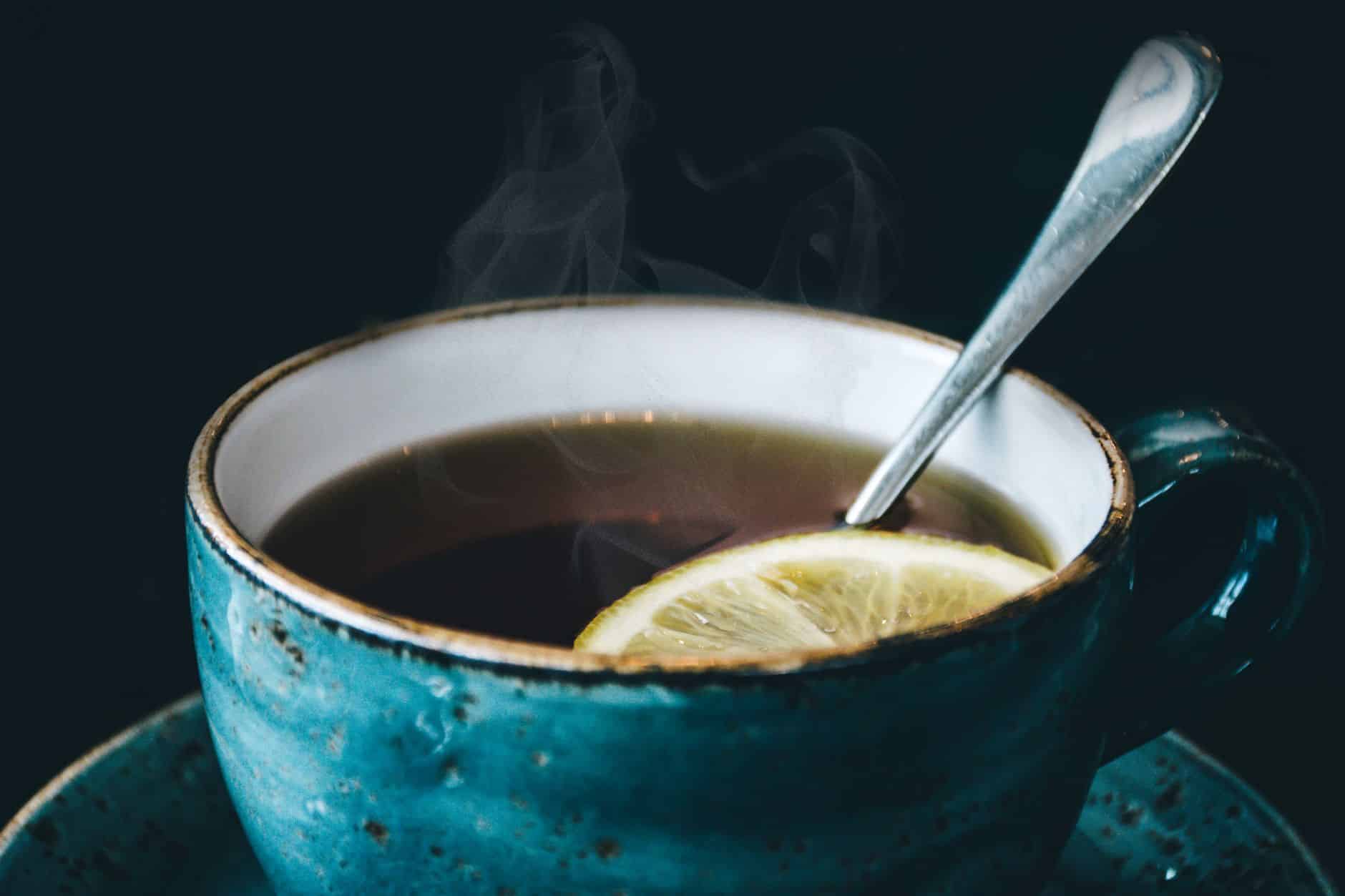 Tasse de tisane à la menthe poivrée fumante avec feuilles fraîches sur table en bois