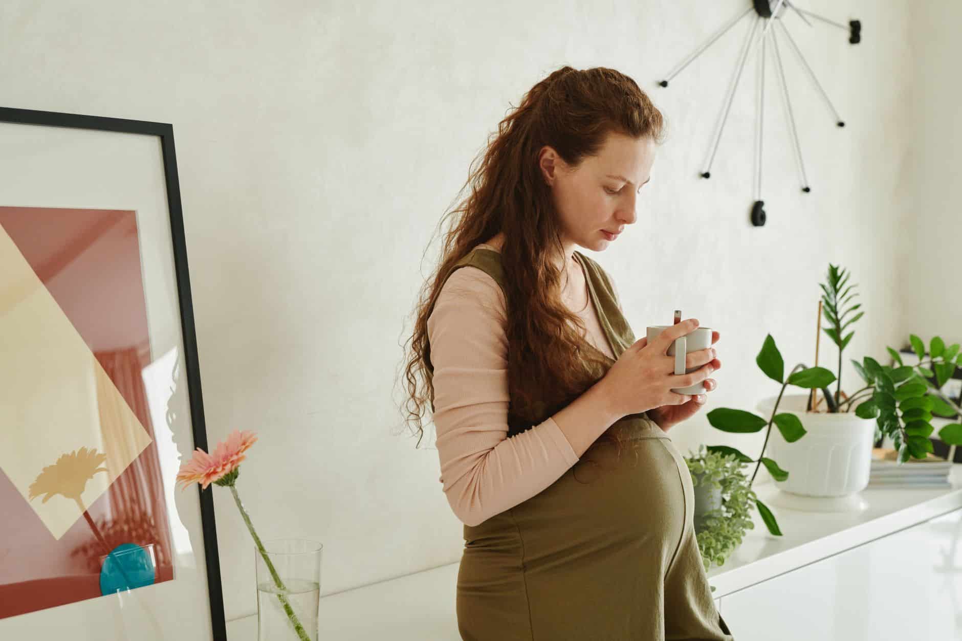 Femme enceinte buvant du rooibos enceinte en cuisine lumineuse